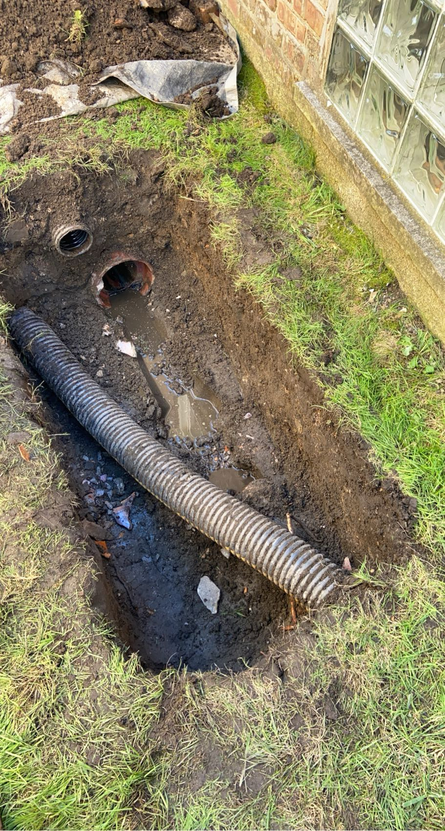 Underground drainage run in Chicago — corrugated pipe laid alongside a brick home